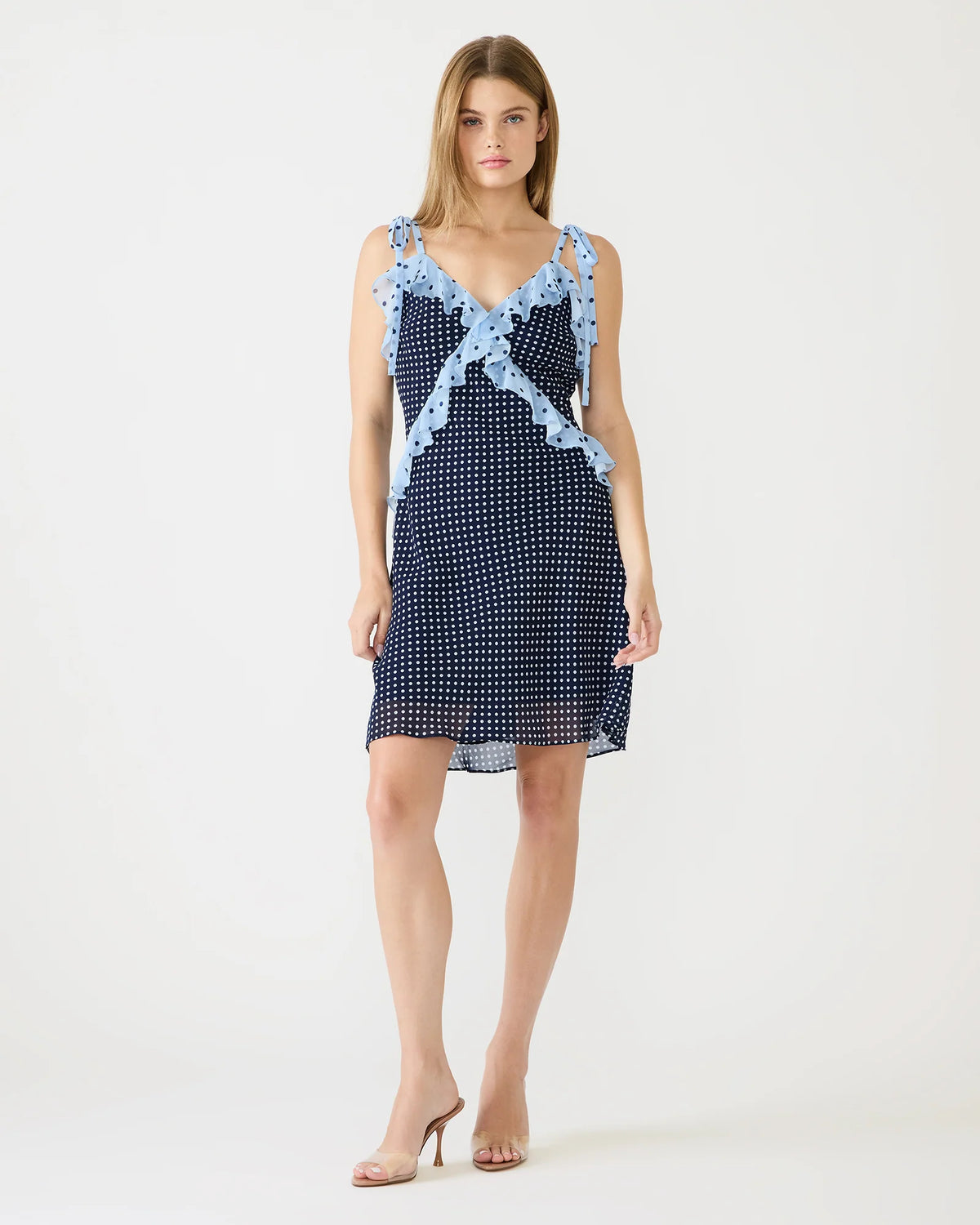 Woman wearing a navy polka dot dress with light blue lace trim on a white background