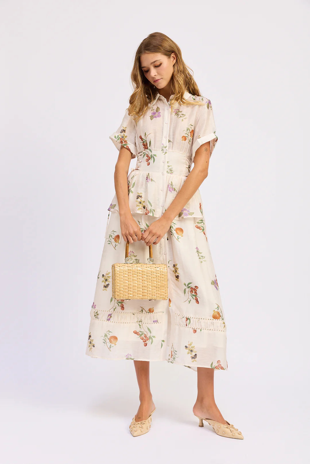 Woman wearing a floral dress holding a woven bag on a white background