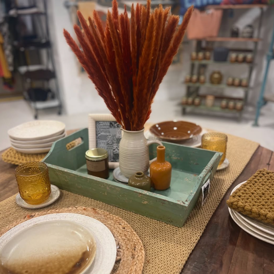 Decorative setting with a green tray, dried plants, and tableware on a wooden table.
