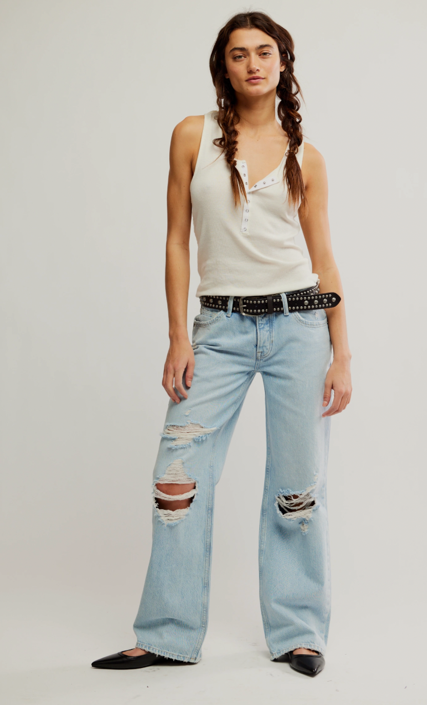 Woman wearing a white tank top and light blue ripped jeans on a plain background