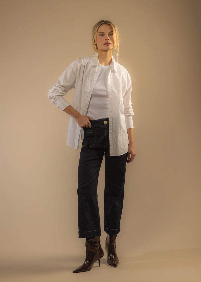 Woman wearing a white shirt, jeans, and brown shoes against a beige background