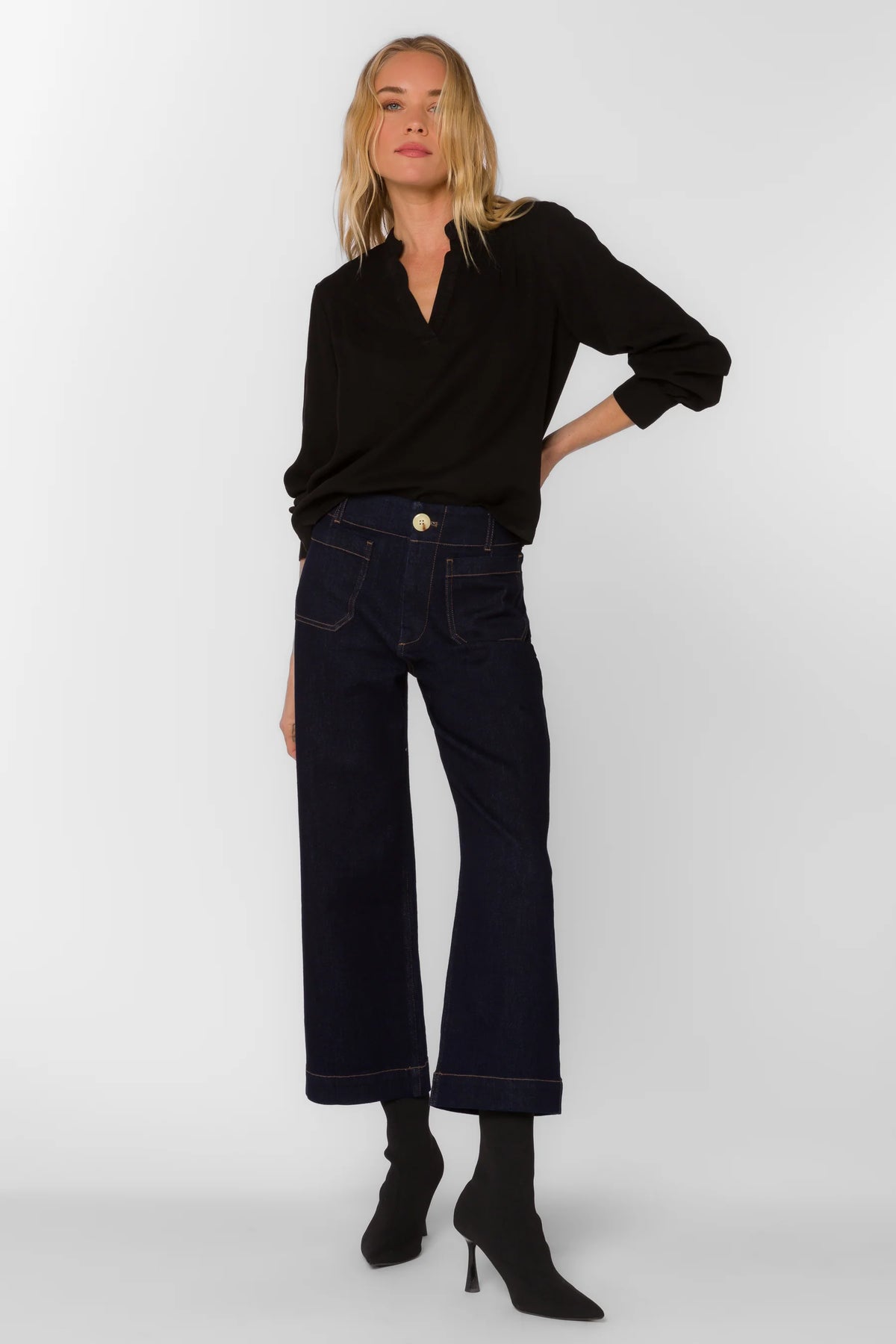 Woman wearing a black top and dark jeans on a white background