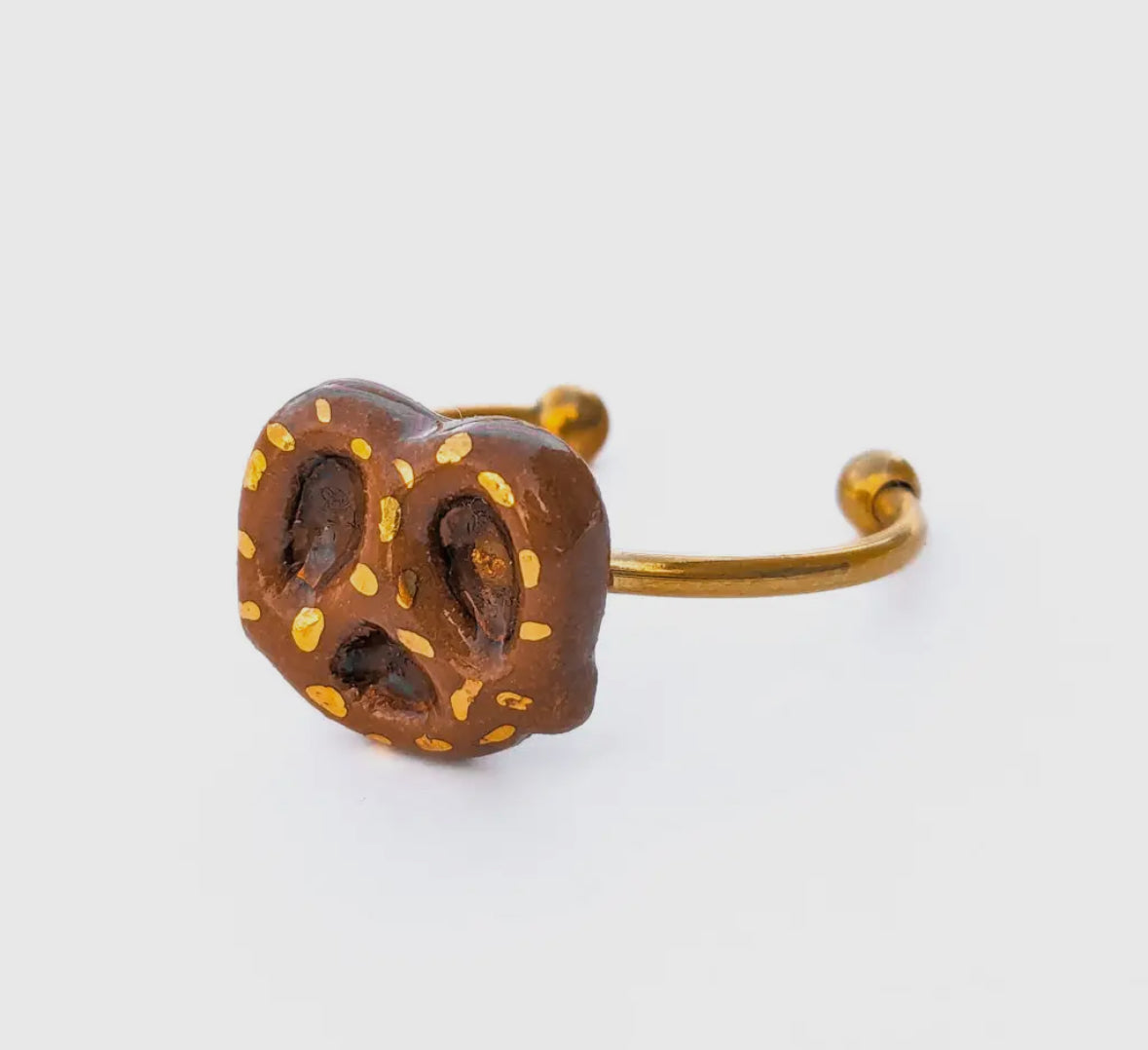 Pretzel-shaped ring with gold accents on a white background