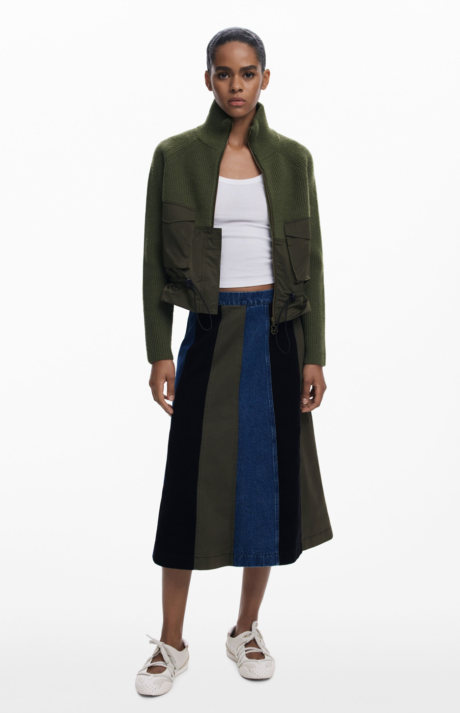Woman wearing a green jacket and a long, multicolored skirt on a white background