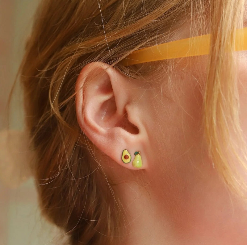 Close-up of an ear wearing avocado-themed earrings with a blurred background