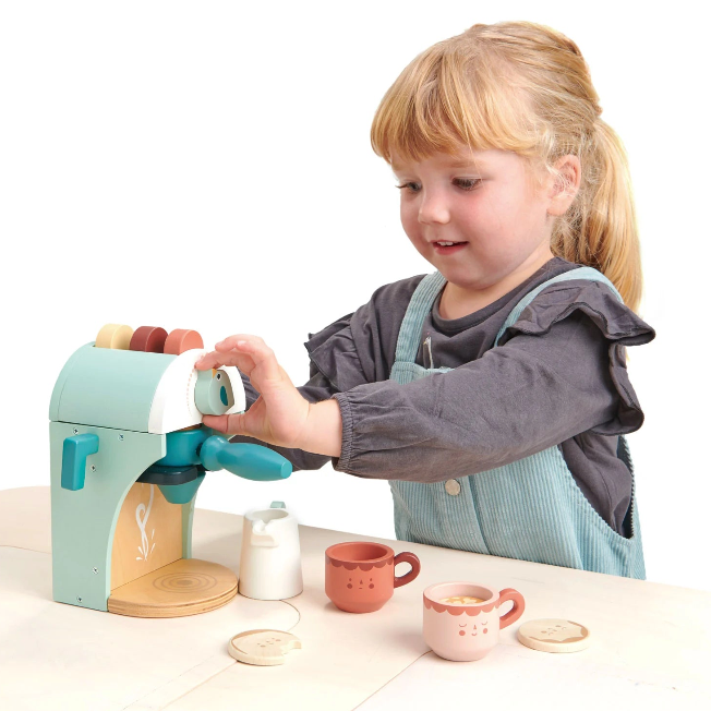 Child playing with a toy coffee machine on a white background