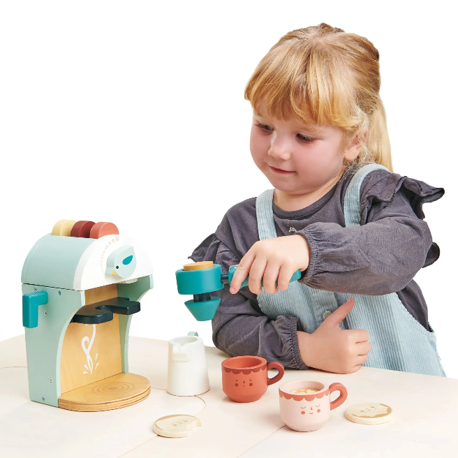 Child playing with a toy coffee maker and cups on a white background