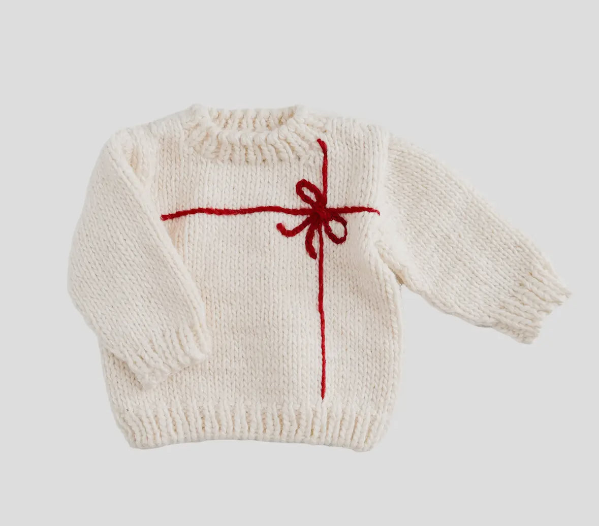 White knitted baby sweater with a red bow design from Blueberry Hill on a light gray background. 