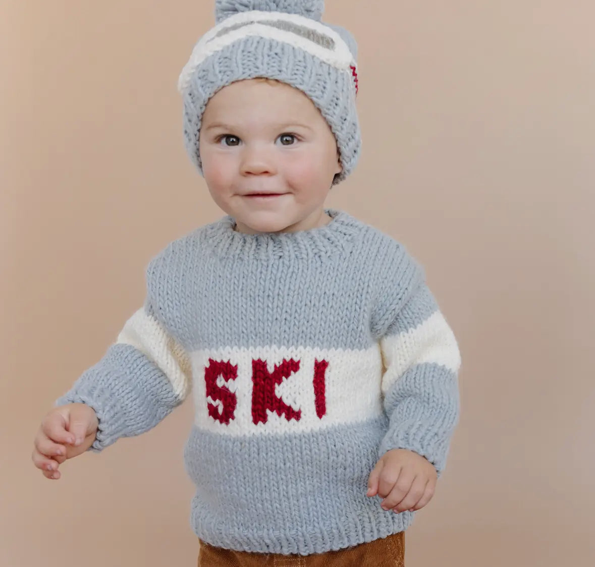 Child wearing a blue knitted sweater with 'SKI' on a beige background