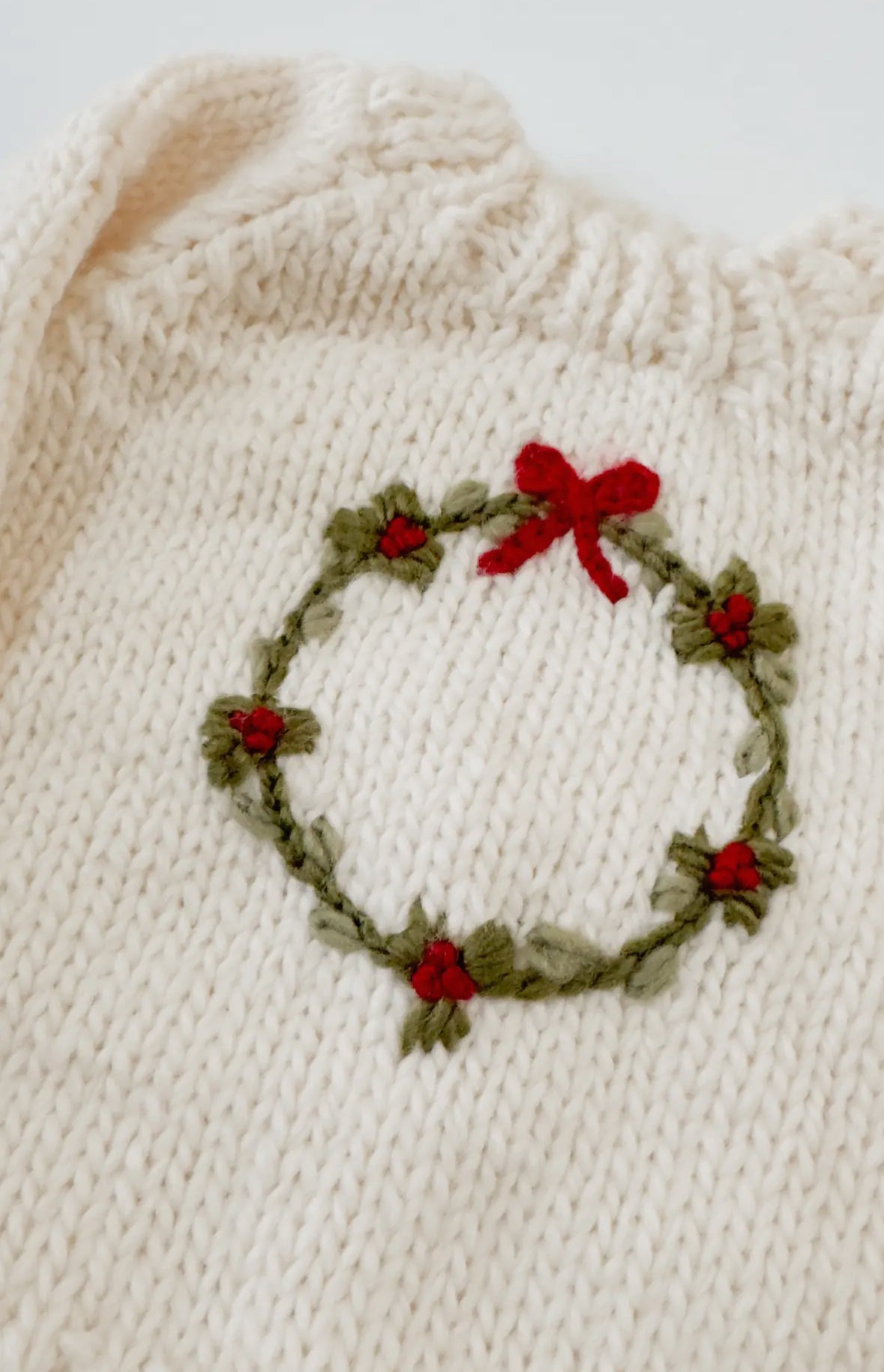 Baby knitted sweater from Blueberry Hill with a Christmas wreath design on a white background. 