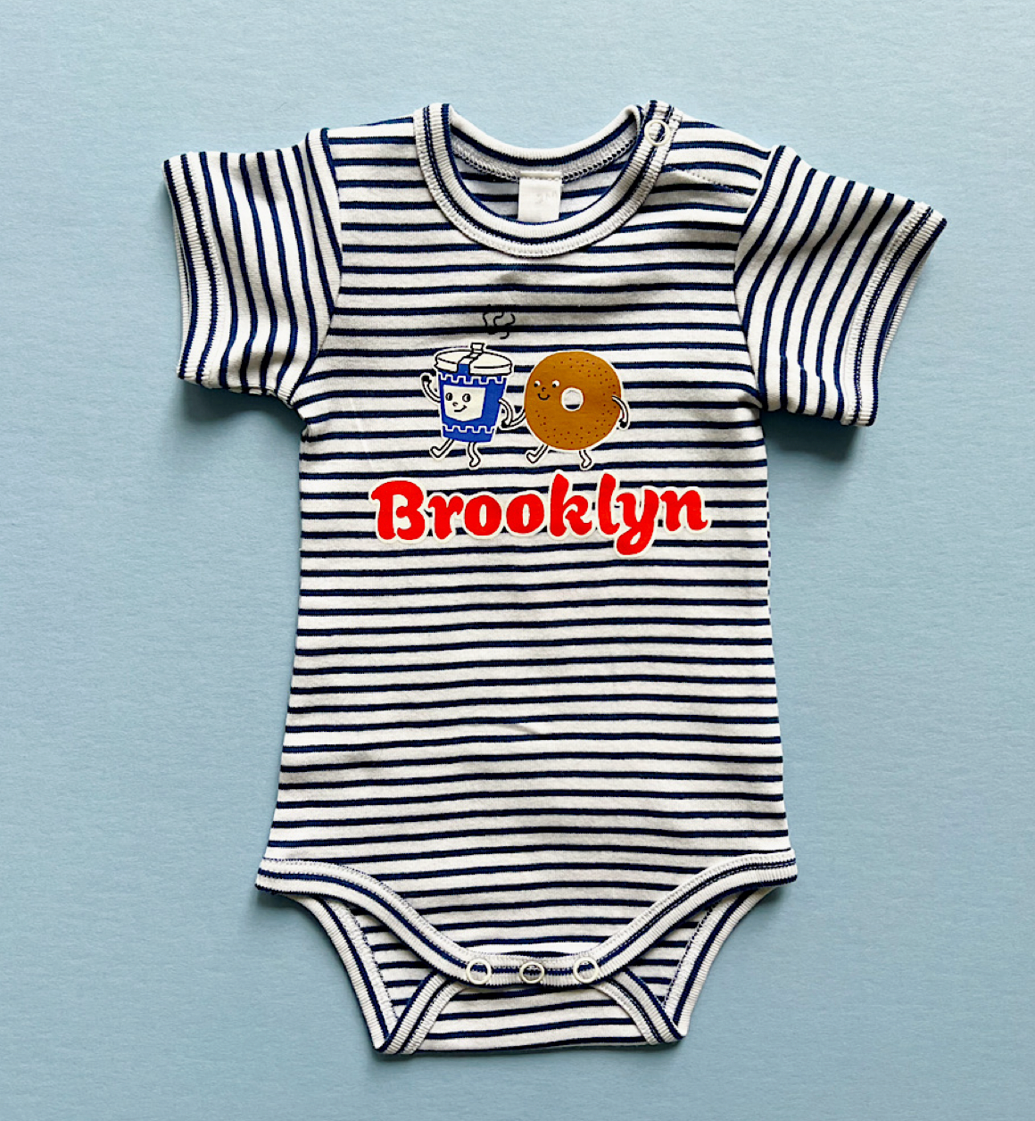 Striped baby onesie with 'Brooklyn' and donut graphic on a blue background