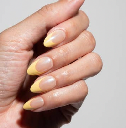 Hand with yellow and white gradient nail polish on a plain background