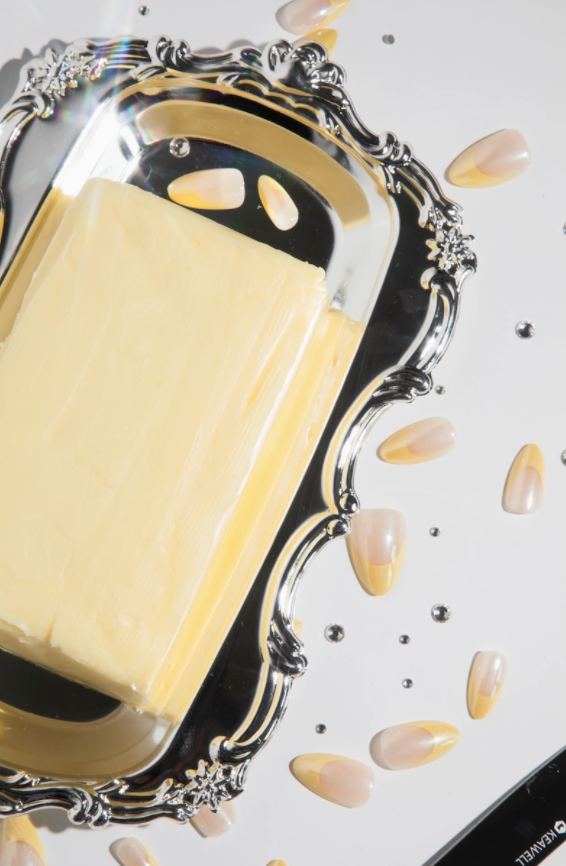 Block of butter on a decorative silver tray with scattered butter pieces on a light background