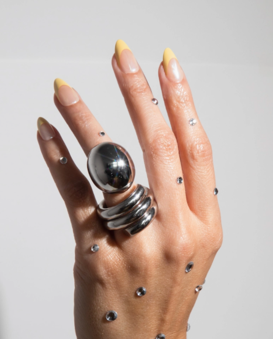 Hand wearing multiple silver rings with a plain background