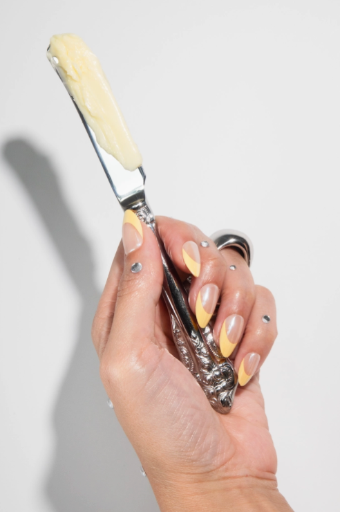 Hand holding a silver tool with a white handle against a light gray background