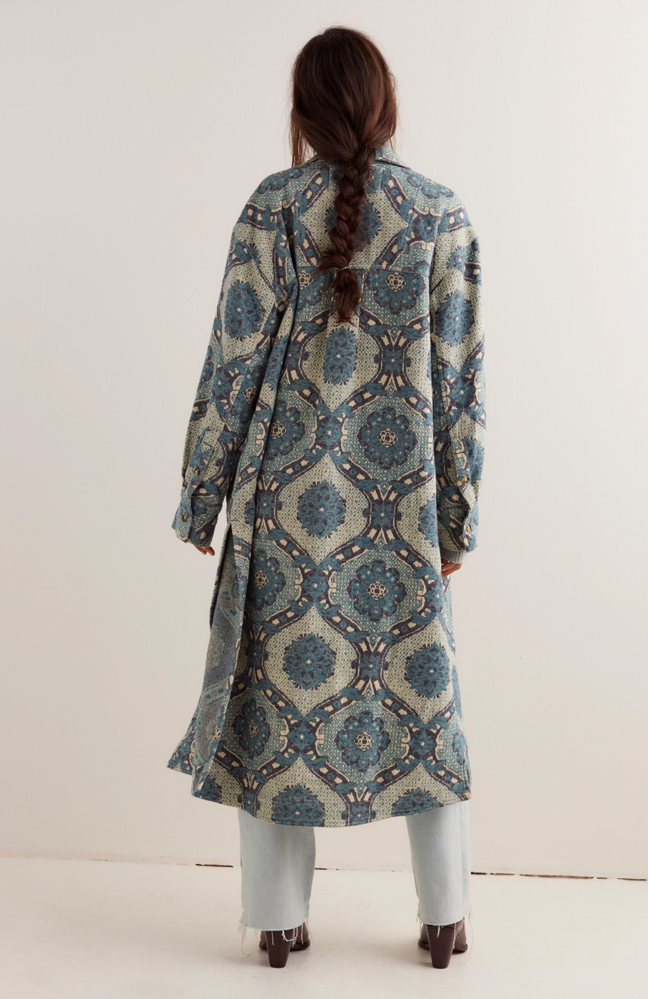 Woman wearing a long, patterned coat with a white background