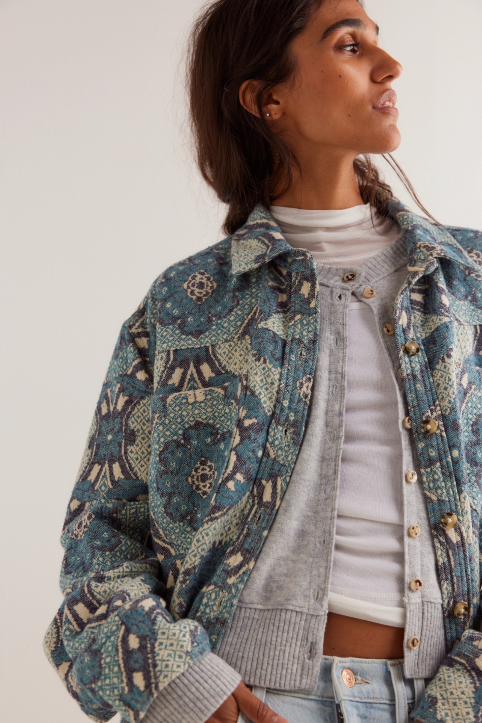 Woman wearing a patterned denim jacket over a white shirt and gray sweater.