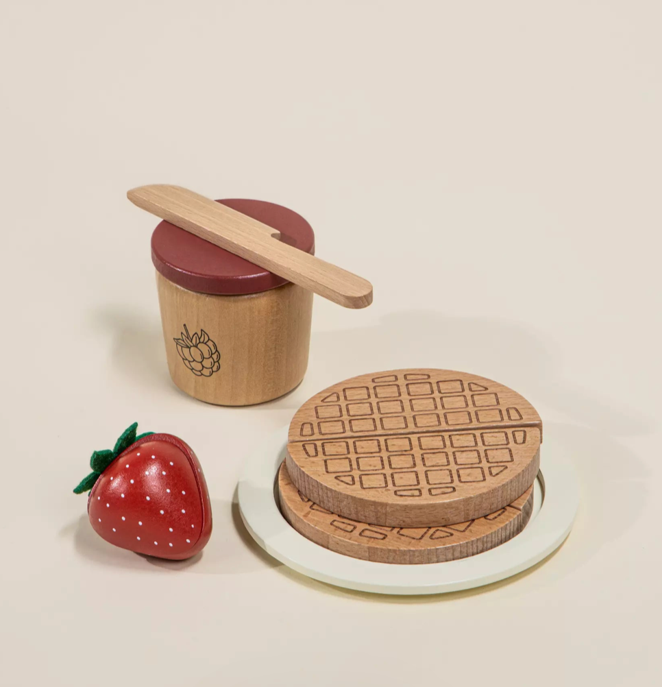 Wooden toy kitchen set with a strawberry, waffle maker, and wooden spoon on a beige background