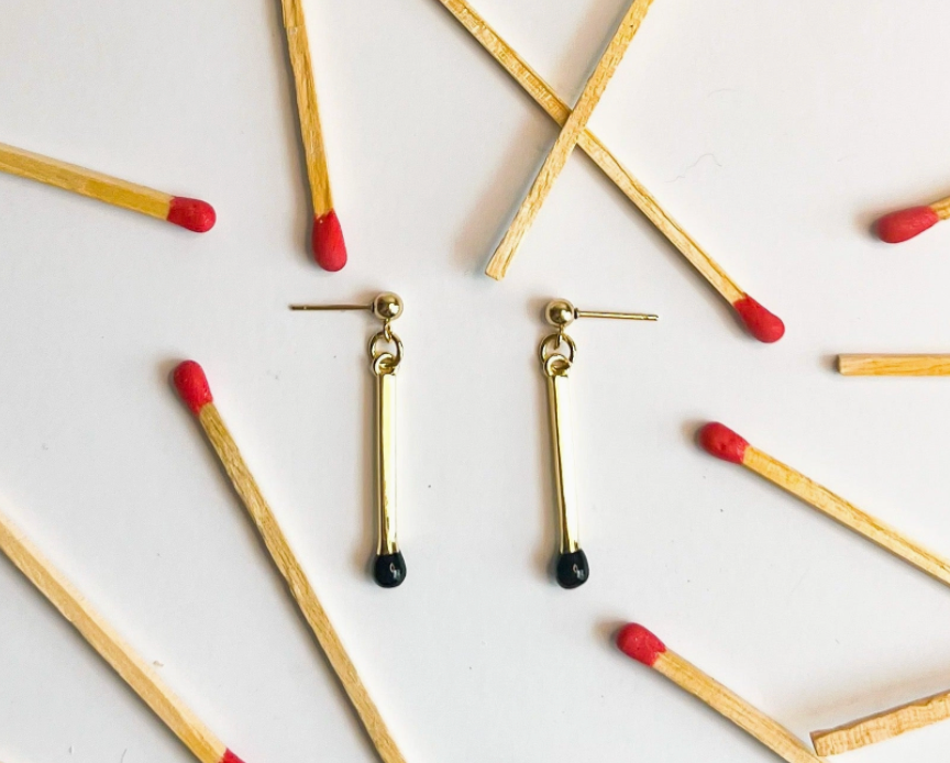 Gold earrings with black and red accents on a white background with matches.