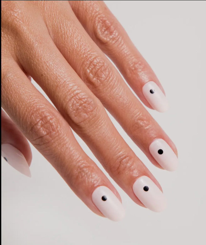 Close-up of a hand with pink nails and black dots on a white background