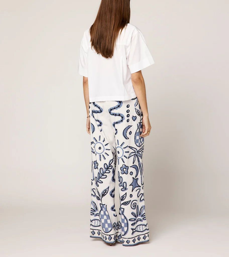 Person wearing a white top and patterned pants on a plain background