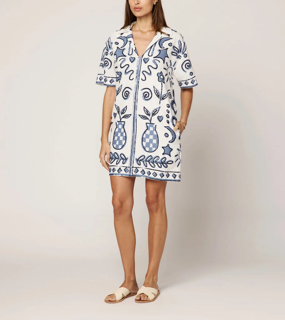 Woman wearing a white dress with blue floral patterns on a plain background