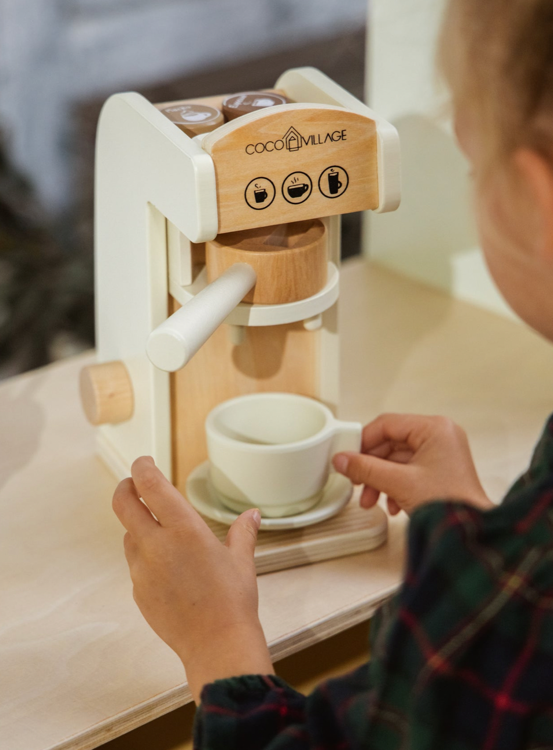 Child playing with a wooden coffee maker toy labeled 'Coco Village' on a table.