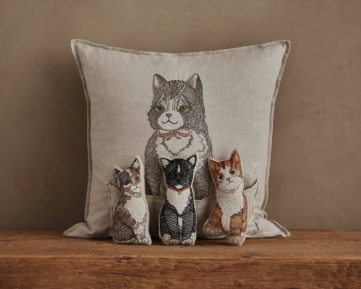 Decorative pillow with embroidered cats on a wooden surface and beige background
