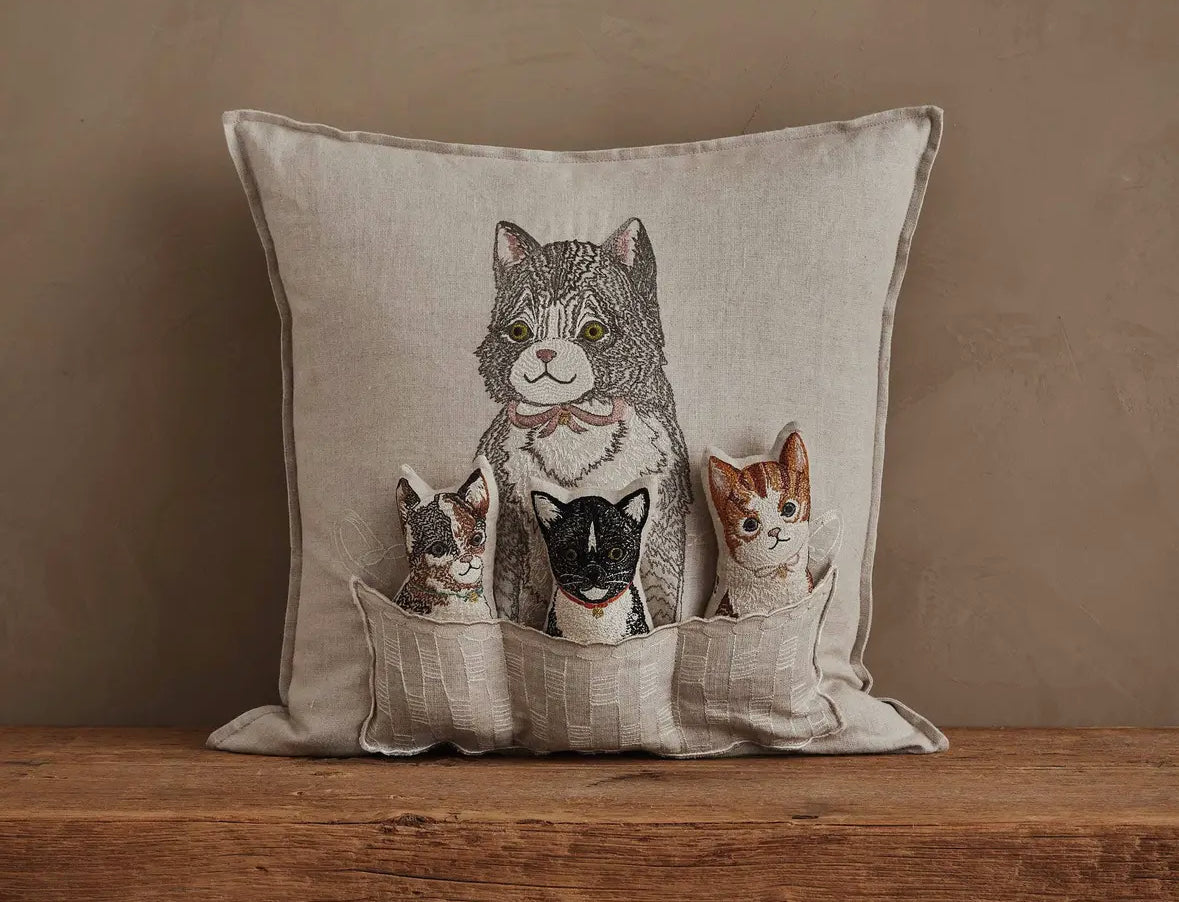 Decorative pillow with embroidered cats on a wooden surface and beige background