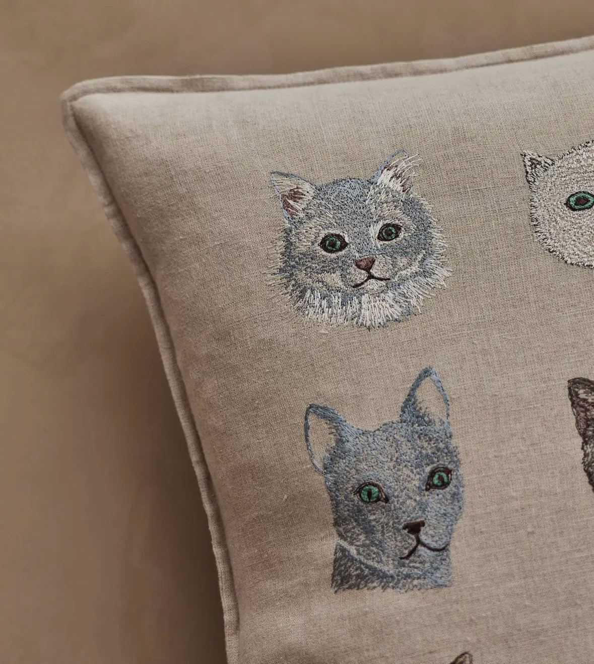 Beige pillow with embroidered cat faces on a beige background
