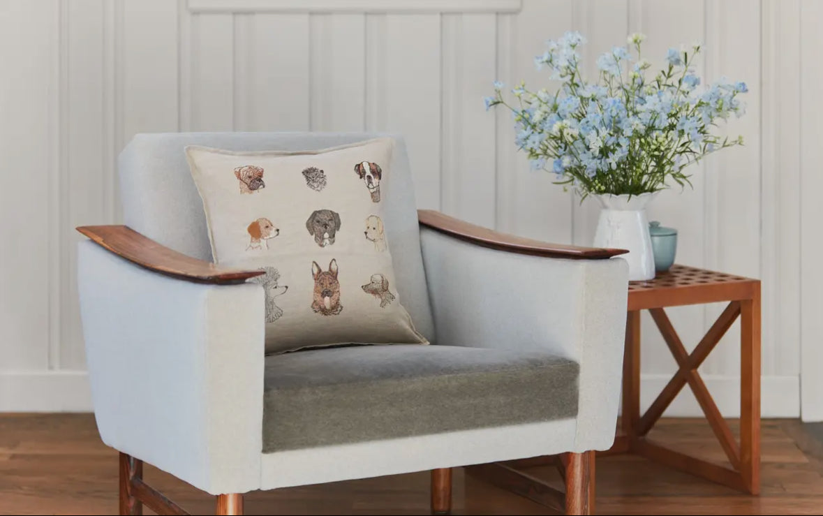 Gray armchair with a decorative pillow featuring animal illustrations, accompanied by a small wooden table with a vase of flowers.