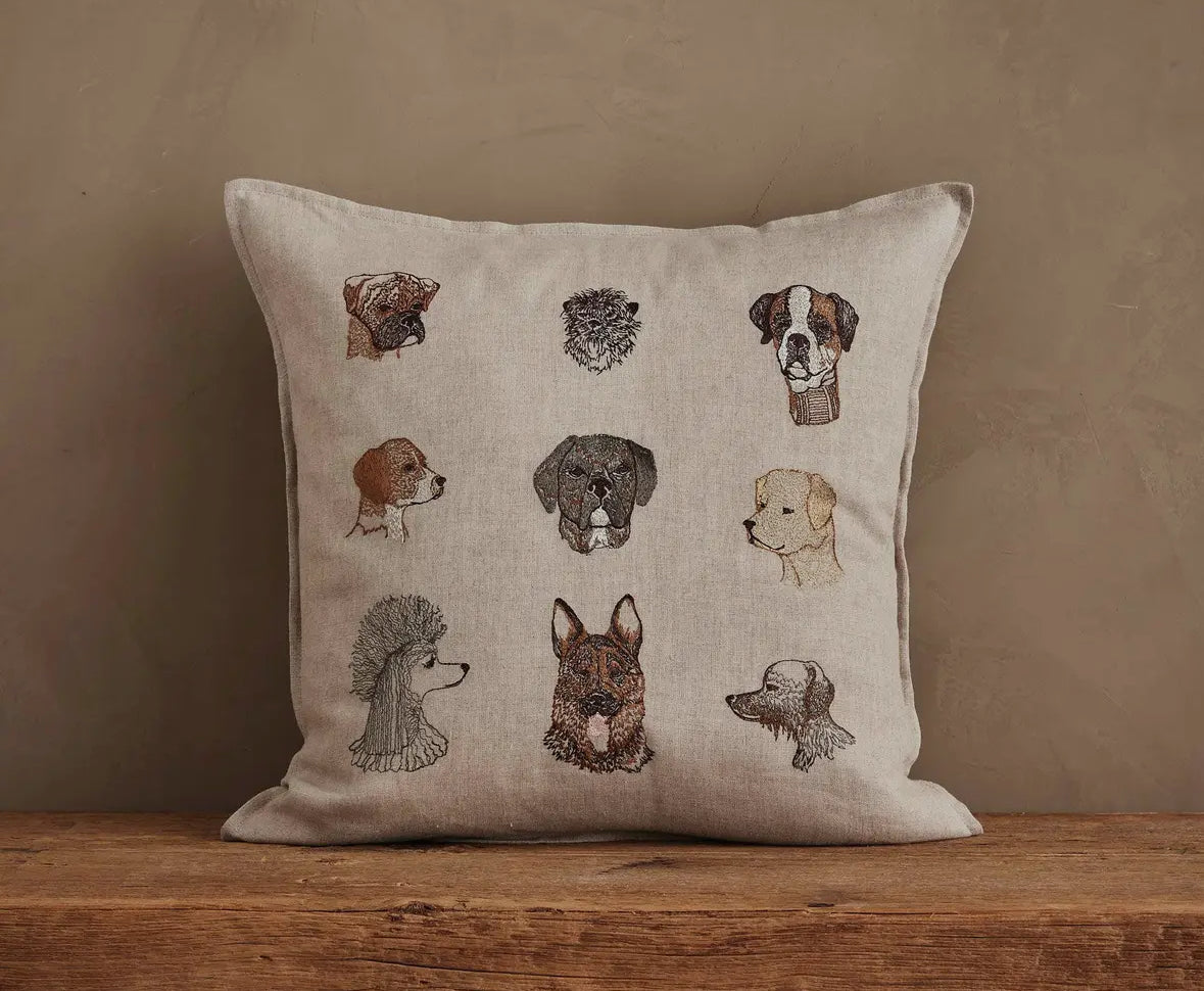 Decorative pillow with embroidered dog faces on a wooden surface and beige background