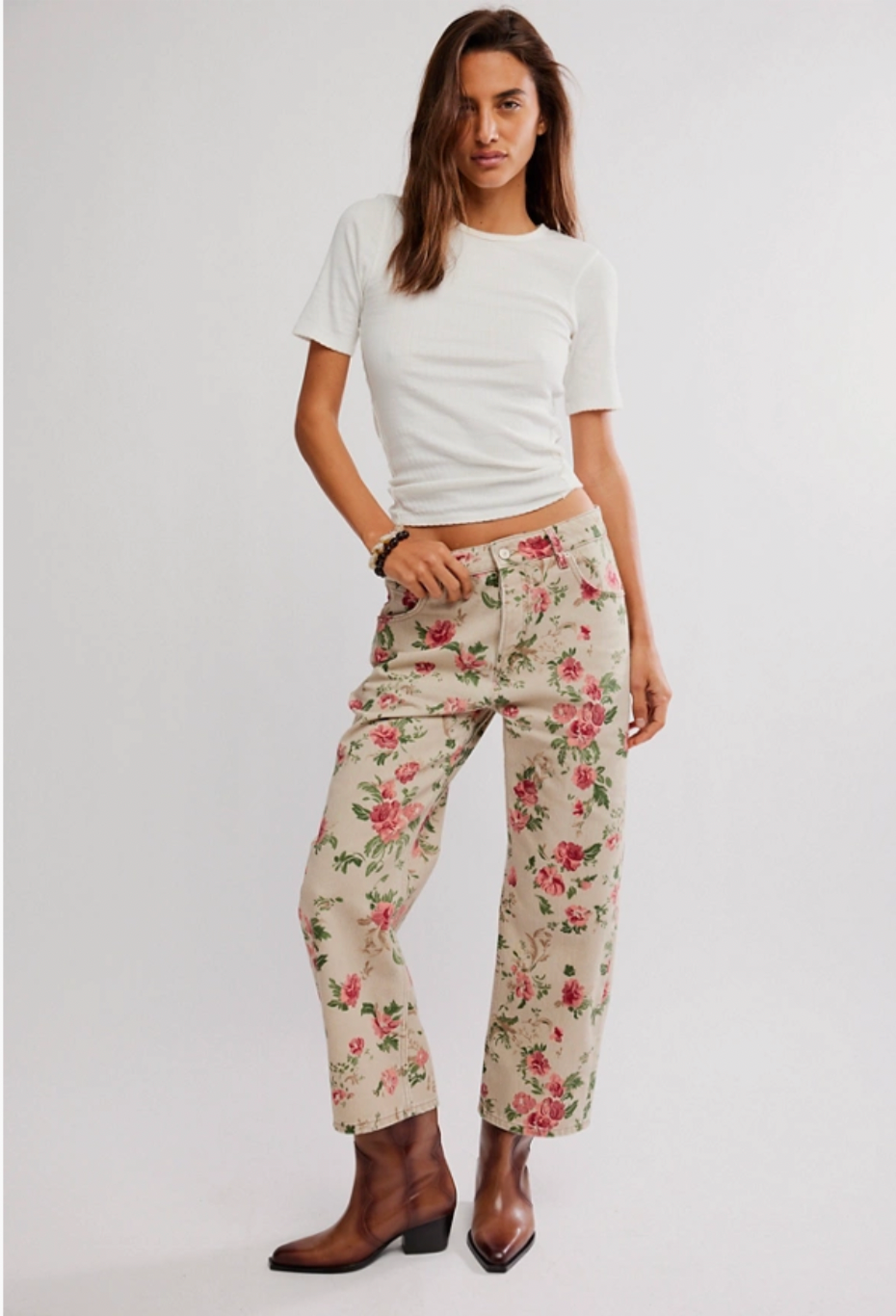 Woman wearing a white crop top and floral pants on a plain background