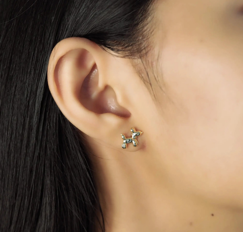 Close-up of an ear wearing a small gold dog-shaped earring with blurred hair and skin in the background.