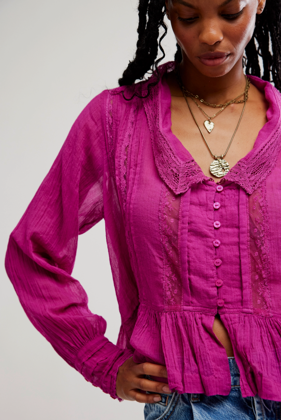 Woman wearing a pink blouse with lace details on a plain background