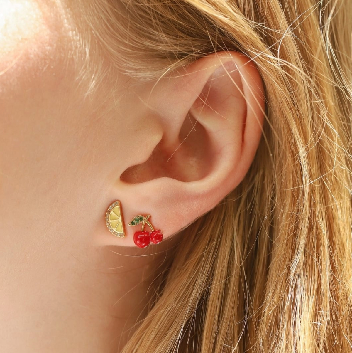 Close-up of an ear wearing a pair of fruit-themed earrings with a blurred background.