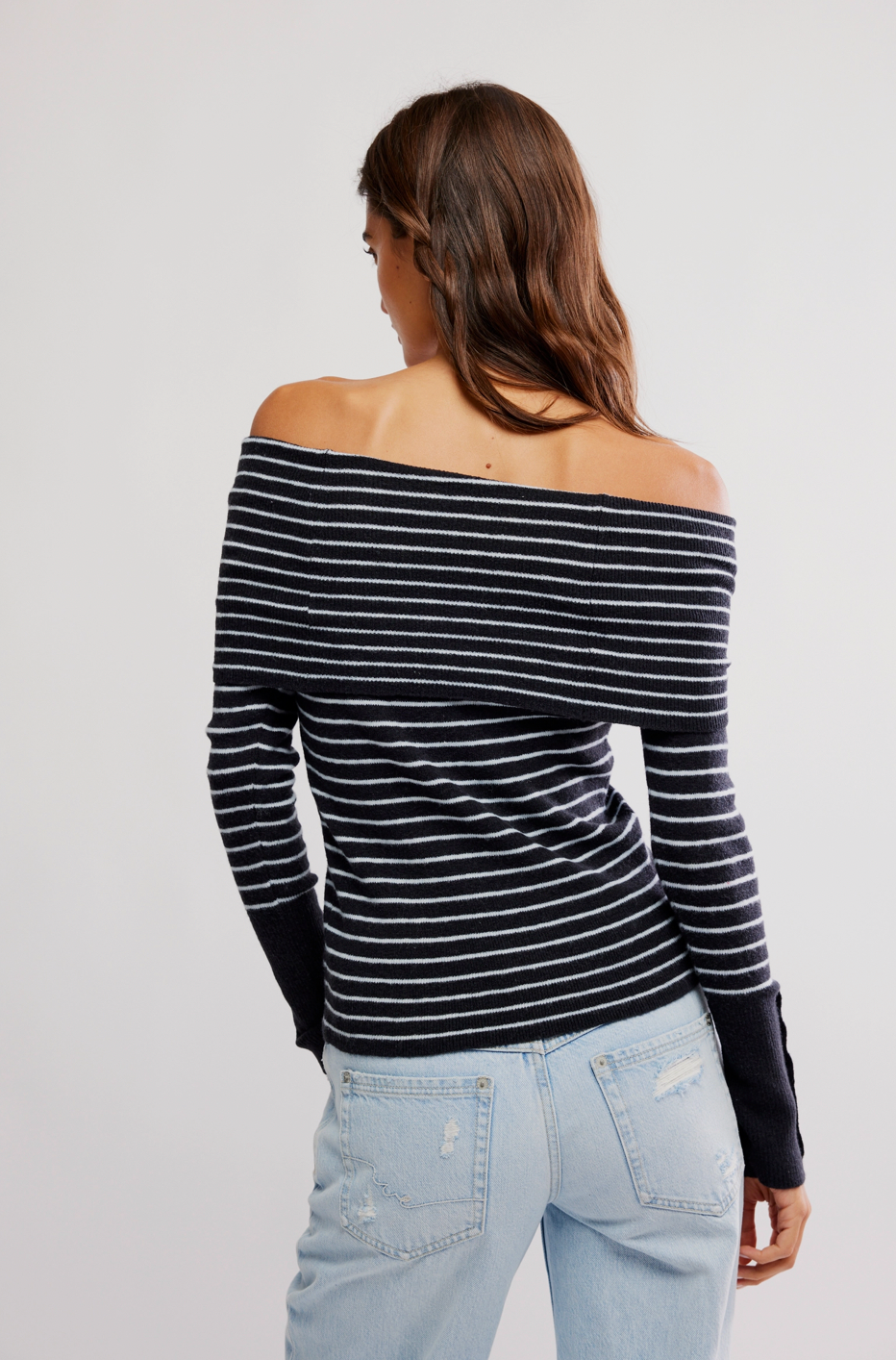 Woman wearing a black and white striped long-sleeve top with light blue jeans on a plain background