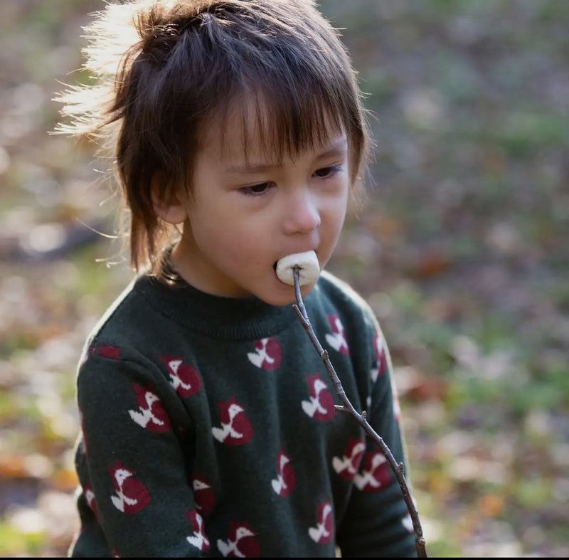 Child eating a marshmallow outdoors with a blurred natural background