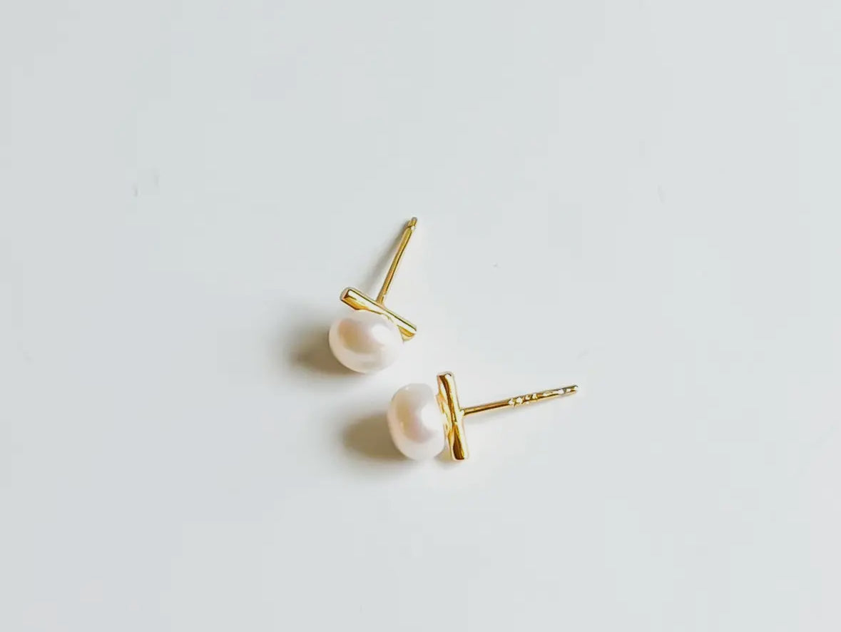 Pair of pearl stud earrings with gold posts on a light gray background