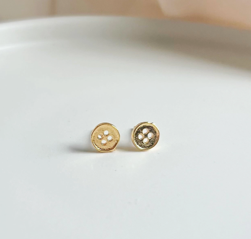Gold earrings on a white surface with a neutral background