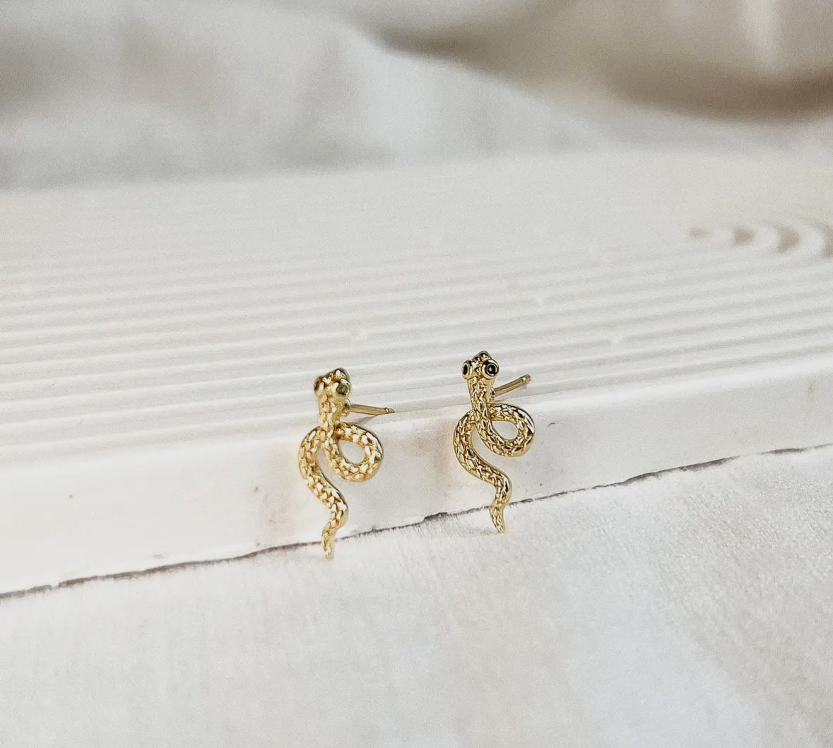 Gold snake-shaped earrings on a textured white surface