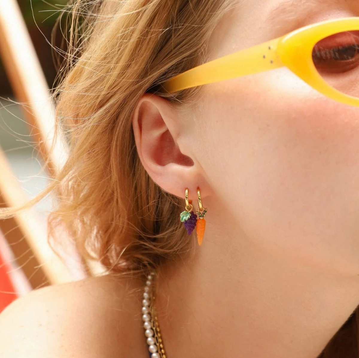 Close-up of a person wearing colorful hoop earrings with yellow sunglasses on.