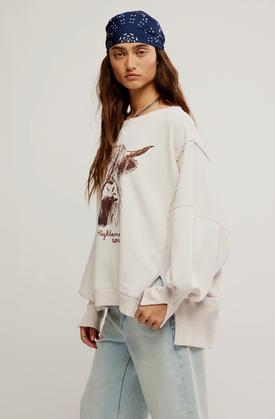 Person wearing a white sweatshirt with a graphic design and a blue bandana on a plain background