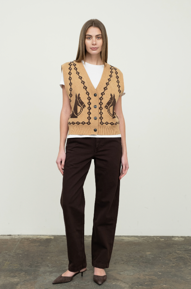 Woman wearing a patterned beige vest and black pants against a white background