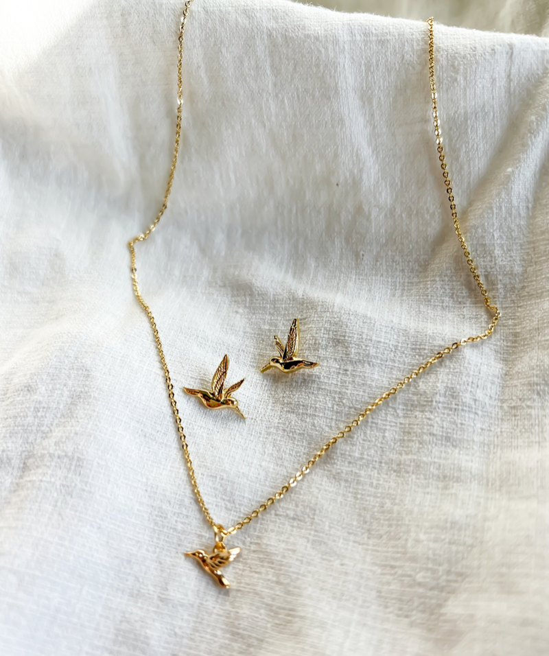 Gold bird-shaped necklace and earrings on a white fabric background