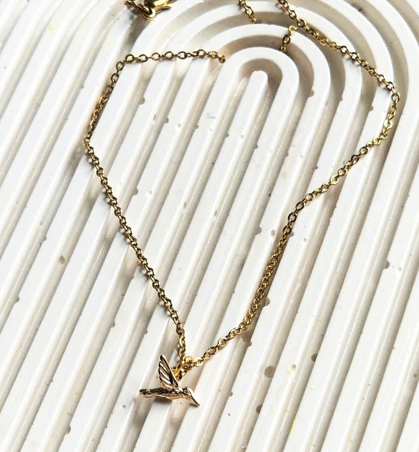 Gold necklace with a bird pendant on a white textured background