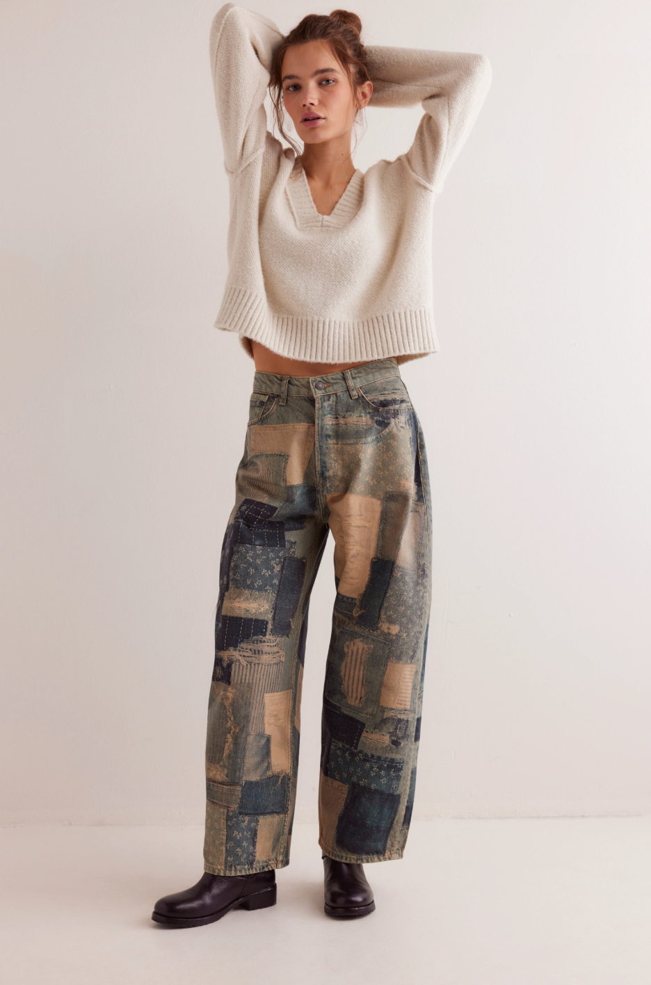 Woman wearing a beige sweater and patchwork pants on a white background