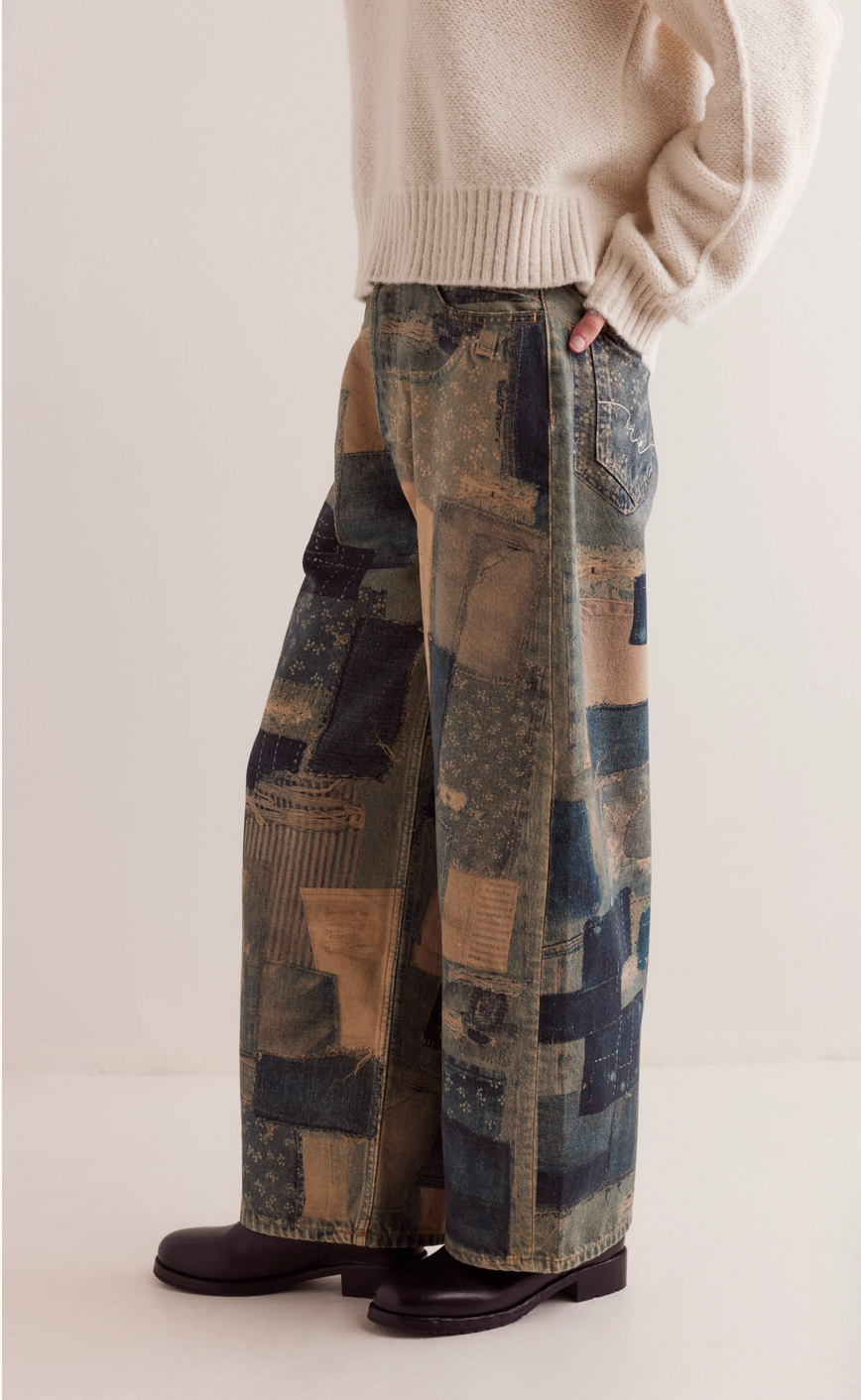 Person wearing a beige sweater and patchwork pants on a white background