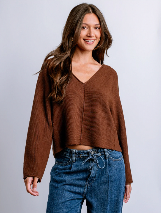 Woman wearing a brown sweater and blue jeans against a plain background
