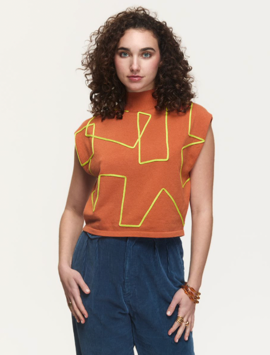 Woman wearing a rust-colored top with yellow geometric patterns on a plain background